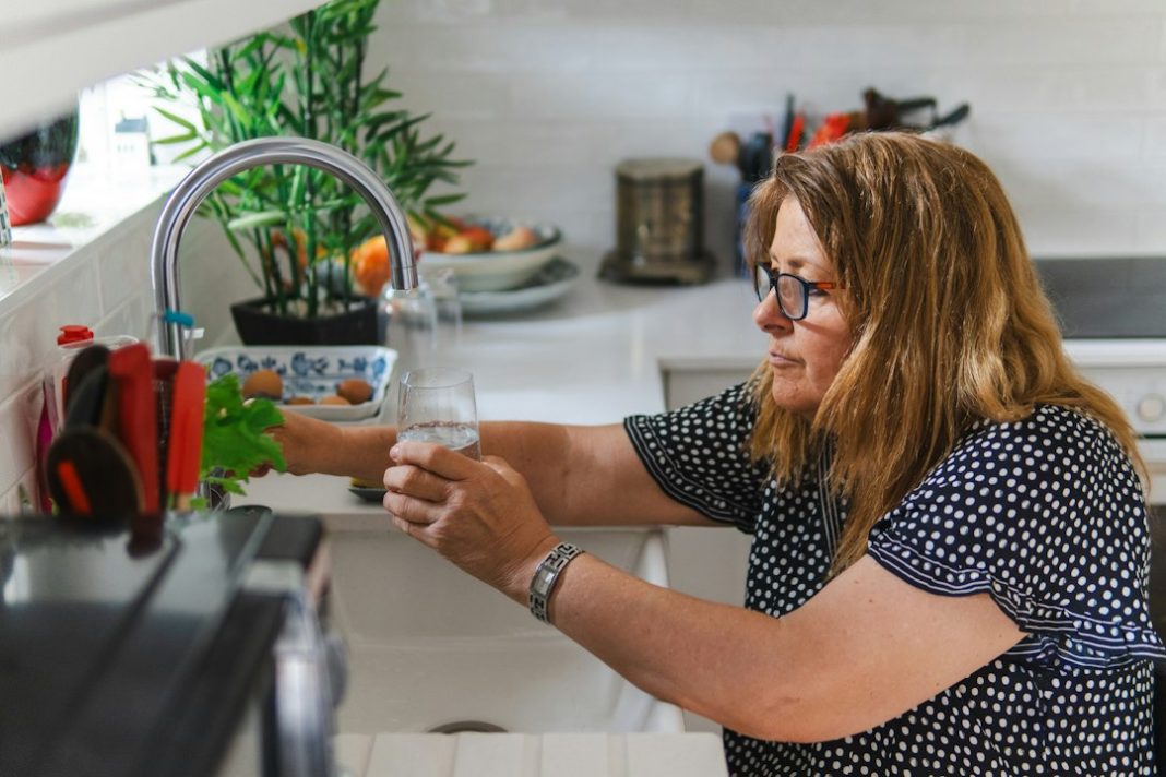 Older woman filling a glass with water at a kitchen faucet